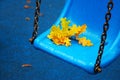 Rainy autumn day in city park. Bright blue park swing in raindrops with yellow oak leaf Royalty Free Stock Photo