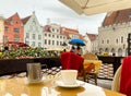 Rainy city Street Cafe Table with cup of coffee and yellow and pink flowers people walk with blue umbrella in Old Town Of Tal