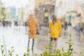Rainy day in city. People seen through raindrops of window. Selective focus on raindrops. Silhouettes of girls in bright Royalty Free Stock Photo