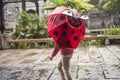 On a rainy day, a little girl with a red beetle-style umbrella is in the scenic spot. Royalty Free Stock Photo