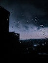 A rainy day, raindrops on the window on cloudy black sky and blurry city buildings background Royalty Free Stock Photo