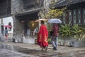 On rainy days, two tourists with umbrellas walked through the scenic spot, one of them wearing a red ancient robe Royalty Free Stock Photo