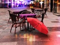 Rainy weather  evening in city street cafe tables empty pink umbrella on old pavement people walking store blurred light Tallinn o Royalty Free Stock Photo