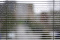 Rainy weather. Wet window with raindrops, blinds and houses out of focus in background