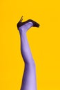 Raised females legs in bright tights and stylish high heels shoes on yellow background