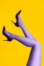 Raised females legs in bright tights and stylish high heels shoes on yellow background