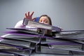 Raised hands of a person who sinks behind stacks of ring binders on an office desk. concept of excessive demands and increasing Royalty Free Stock Photo