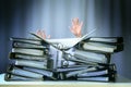 Raised hands of a person who sinks behind stacks of ring binders on an office desk, concept of excessive demands and increasing Royalty Free Stock Photo