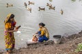 Rajshahi, Bangladesh - July 6, 2016: Two women washing colourful saris in a lake with ducks