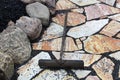A rake being used to place black pebbles between patio stones