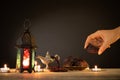 Ramadan food and drinks concept. Woman hand reaches out to a plate with date with Ramadan Lantern with arabian lamp, wood rosary,