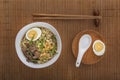 Ramen soup with chicken, noodles, egg and sprouted beans on a white plate on a bamboo mat with a spoon and chopsticks. Royalty Free Stock Photo