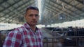 Rancher standing modern cowshed looking camera close up. Portrait farm employee.