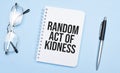 random act of kidness words in white notepad, pen and glasses on blue background. Concept
