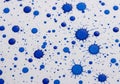 Random blue ink splatters of varying sizes cover a white textured paper surface. The splatters Royalty Free Stock Photo