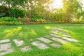 Random pattern of grey concrete stepping stone on green grass lawn, Flowering plant, shurb and trees on background under morning Royalty Free Stock Photo