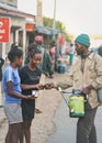 Ranohira, Madagascar - April 29, 2019:  Unknown Malagasy man selling fruit drink to two young girls on street, pouring it directly Royalty Free Stock Photo