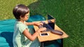 Asian girl look at laptop learning from home with smartphone and camera in the front yard.