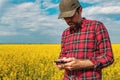 Rapeseed crop farmer using smartphone in blooming canola field.