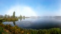 Rare landscape with a rainbow of fog in the early autumn morning, lake shore, traditional lake meadow vegetation in the foreground Royalty Free Stock Photo