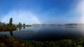 Rare landscape with a rainbow of fog in the early autumn morning, lake shore, traditional lake meadow vegetation in the foreground Royalty Free Stock Photo