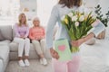 Rare view photo of little girl keeping postcard tulips bunch hiding behind back to congratulate mother granny