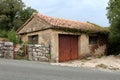 Rarely used old garage with rusted metal doors and small windows partially overgrown with crawler plant next to stone wall and