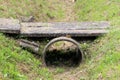 Rarely used small improvised bridge made from long concrete tiles over overgrown storm drain concrete pipe covered with uncut