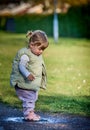 Rascal little female child with braids jumping in a muddy puddle on a sunny spring day. Scoundrel 2 year old girl Royalty Free Stock Photo