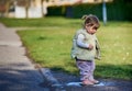 Rascal little female child with braids jumping in a muddy puddle on a sunny spring day. Scoundrel 2 year old girl