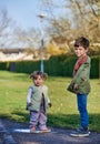 Rascal siblings or children: young 7 years old brother supports 2 year old sister jumping in a muddy puddle. Two bonding brothers