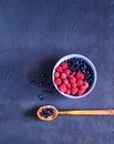 Raspberries and bilberry in blue bowl on blue background.