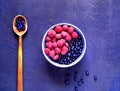 Raspberries and bilberry in blue bowl on blue background. Berry picking, organic food concept.