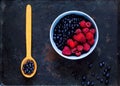 raspberries and bilberry in blue bowl on vintage rusty metal background. Berry picking, organic food concept,