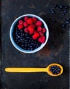 raspberries and bilberry in blue bowl on vintage rusty metal background. Berry picking, organic food concept, flat lay