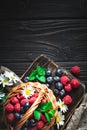 Raspberries and blueberries in a basket with chamomile and leaves on a dark background. Summer and healthy food concept