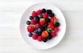 raspberries, strawberries, blackberries, wild strawberries, blueberries on white plate on white wooden table for food card design Royalty Free Stock Photo