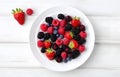 raspberries, strawberries, blackberries, wild strawberries, blueberries on white plate on white wooden table for food card design Royalty Free Stock Photo