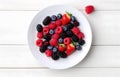 raspberries, strawberries, blackberries, wild strawberries, blueberries on white plate on white wooden table for food card design Royalty Free Stock Photo