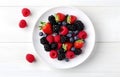 raspberries, strawberries, blackberries, wild strawberries, blueberries on white plate on white wooden table for food card design Royalty Free Stock Photo