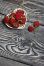 Raspberries with tails lie in a heart-shaped saucer. Several berries are nearby. On black boards, with an expressive woody texture