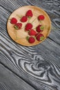 Raspberries with tails lie on a wooden saucer. On black boards, with an expressive woody texture