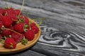 Raspberries with tails lie on a wooden saucer. On black boards, with an expressive woody texture