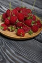 Raspberries with tails lie on a wooden saucer. On black boards, with an expressive woody texture