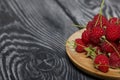 Raspberries with tails lie on a wooden saucer. On black boards, with an expressive woody texture