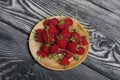 Raspberries with tails lie on a wooden saucer. On black boards, with an expressive woody texture