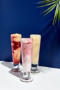 Raspberry and banana, pineapple, strawberry and coconut milk smoothie over white and blue background. Palm leaf with sunshine and Royalty Free Stock Photo