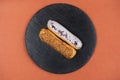 Raspberry and caramel eclair on round black rock stand on brown background. Eclairs with white glaze in cafe. View from