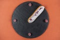 Raspberry eclair on round black rock stand on brown background. Eclair with white glaze and raspberries in cafe. View