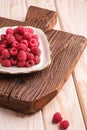 Raspberry fruits in plate on old teak cutting board, healthy pile of summer berries on wooden background Royalty Free Stock Photo